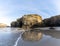 Sandy beach panorama with tidal pools and jagged broken cliffs behind in warm evening light