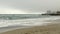 Sandy beach and rough sea,pier and high-rise hotel building in fog,dense clouds