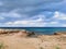 The sandy coast of the Mediterranean Sea, turning into stones from a long-hardened lava, azure water against a dramatic sky