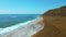 Sandy dunes overgrown with yellow grass on ocean coastline. Clip. Aerial view of burnt meadow and turquoise ocean.