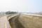 Sandy ground between footbridge and canal in sunny foggy winter