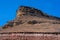 Sandy mountain with a sharp cliff and a small amount of vegetation against the blue sky