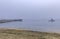 Sandy Pacific Ocean beach and a fishing pier in Half Moon Bay near San Francisco on a foggy day, boats in the background