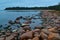 Sandy red stones coast of blue bay of Ladoga Lake in autumn, with trees on horizon