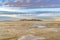 Sandy shore of a lake and distant rugged mountain under cloudy blue sky