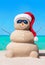 Sandy snowman in Christmas hat and sunglasses at tropical beach