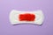 Sanitary pad with red feather on violet background
