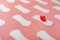 Sanitary pads on a pink background in the form of a diagonal pattern of repetitions, with a red flower on the pad