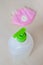 Sanitizer bottle with green dispenser and pink reusable antiviral protective mask in blur, view from above