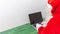 Santa Claus` back shot working on a laptop on a green wooden desk