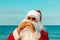 Santa Claus on the beach eating a hamburger.