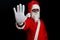 Santa claus on black background with serious face raises his arm and makes the stop sign with his hand.