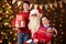 Santa Claus and child boy and girl posing together indoor near decorated xmas tree with lights, they talking, smiling and