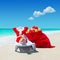 Santa Claus with Christmas sack full of gifts relax on sunlounger barefooted at perfect sandy ocean beach.