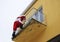 A Santa Claus climbing to a terrace of a yellow building funny horizontal