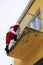 A Santa Claus climbing to a terrace of a yellow building funny vertical