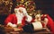 Santa Claus at desk with letters, gifts near Christmas tree