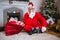 Santa claus with gift sack sitting on rug with finger on lips in living room