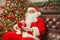 Santa Claus with giftbox on background of sparkling firtree. Christmas