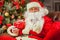 Santa Claus with giftbox on background of sparkling firtree. Christmas