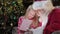 Santa Claus gives young blonde girl gift box with lighting gift. Girl opens gift with Santa Claus, bright light shines