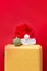 Santa Claus hat lies on yellow suitcase with christmas bauble on red background. Concept: tourist trips, vacation, travel during