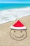 Santa Claus hat and smiley face on seashore against waves