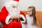 Santa Claus helps to untie ribbon gift, little girl happily looking at him