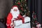 Santa Claus is holding christmas present box with fully decorated chrsitmas tree for season celebration and happy new year event