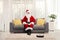 Santa claus at home sitting on a sofa and a robotic vacuum cleaner cleaning on the floor