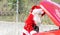 Santa Claus looking at the engine of his damaged car at Christmas