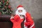 Santa Claus is playing peek a boo with little toddler baby in the house with fully decorated christmas tree for season celebration