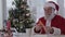 Santa Claus read wish letters sitting at table near Christmas tree