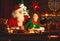 Santa claus reads letter to little elf by Christmas tree