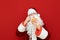 Santa Claus in red costume and beard isolated on red background, holds a tasty burger in his hands and is about to eat it. Funny