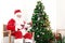 Santa Claus in red costume playing Ukulele and singing Christmas songs front of decorative Christmas tree in living room. Happy