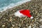 Santa Claus red hat and beard lie on sea shore on pebbles, Christmas concept and travel