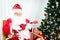 Santa Claus sitting on chair and playing Ukulele, singing Christmas songs front of decorative Christmas tree in living room, Merry