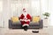 Santa claus sitting on a sofa with a gift box and a robotic vacuum cleaner dusting