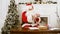 Santa Claus sitting at the table in his Christmas workshop signing presents for children