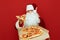 Santa Claus stands on red background with pizza box and piece in hand and looks into camera. Santa eats hot pizza from delivery,