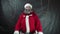 Santa claus thumbs up on dark gray background. Strange middle-aged man with gray beard in Christmas costume likes with