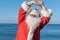 Santa doing exercises on the ocean. Traditional red outfit and relaxing on the beach