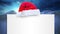 Santa hat over a blank placard against snow falling on winter landscape