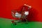 Santa hat in shopping trolley on isometric red green background. Online shopping holiday concept Copy space for your