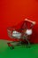 Santa hat in shopping trolley on isometric red green background. Online shopping holiday concept Copy space for your