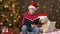 Santa helper boy reading book to bear toy, sitting indoor near decorated xmas tree with lights - Merry Christmas and Happy Holiday