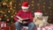 Santa helper boy reading book to bear toy, sitting indoor near decorated xmas tree with lights - Merry Christmas and Happy Holiday