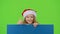 Santa helper jumps out from behind the blue board and shows a thumbs up. Green screen