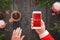 Santa holding smart phone with Merry Christmas message on screen and drink hot tea